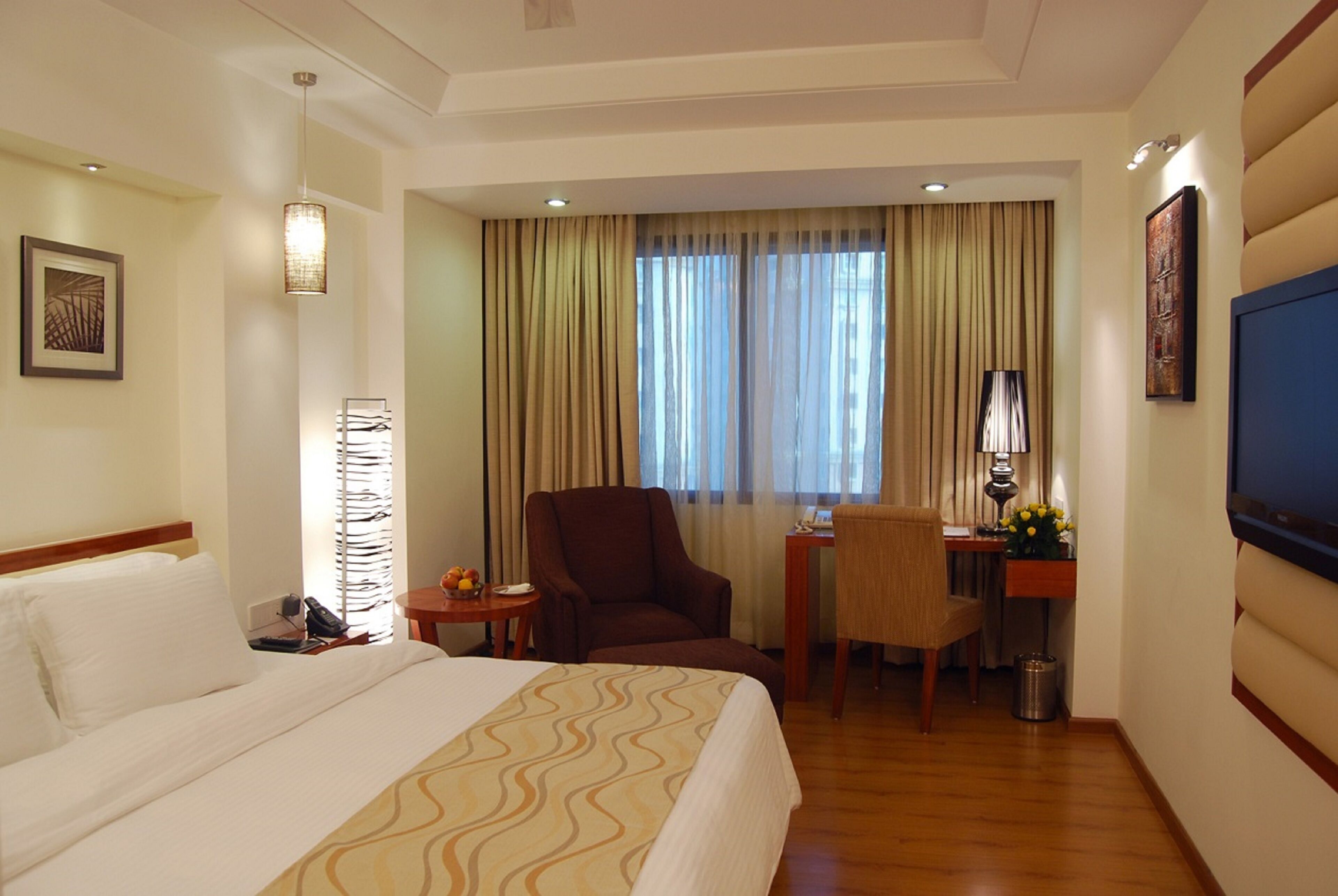 A hotel room with a bed, a desk, a chair, a lamp, and a TV.