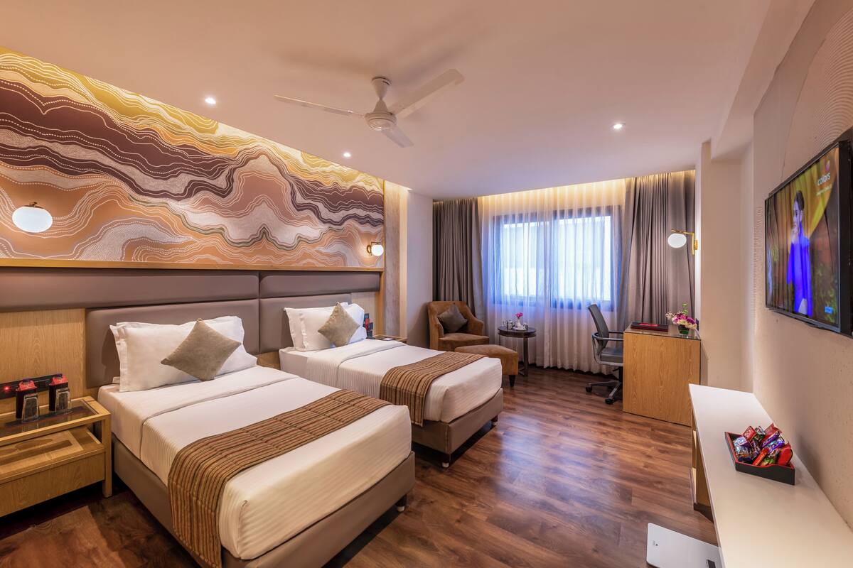 Habitación de hotel con dos camas, un escritorio, una silla, un televisor y un ventilador de techo.