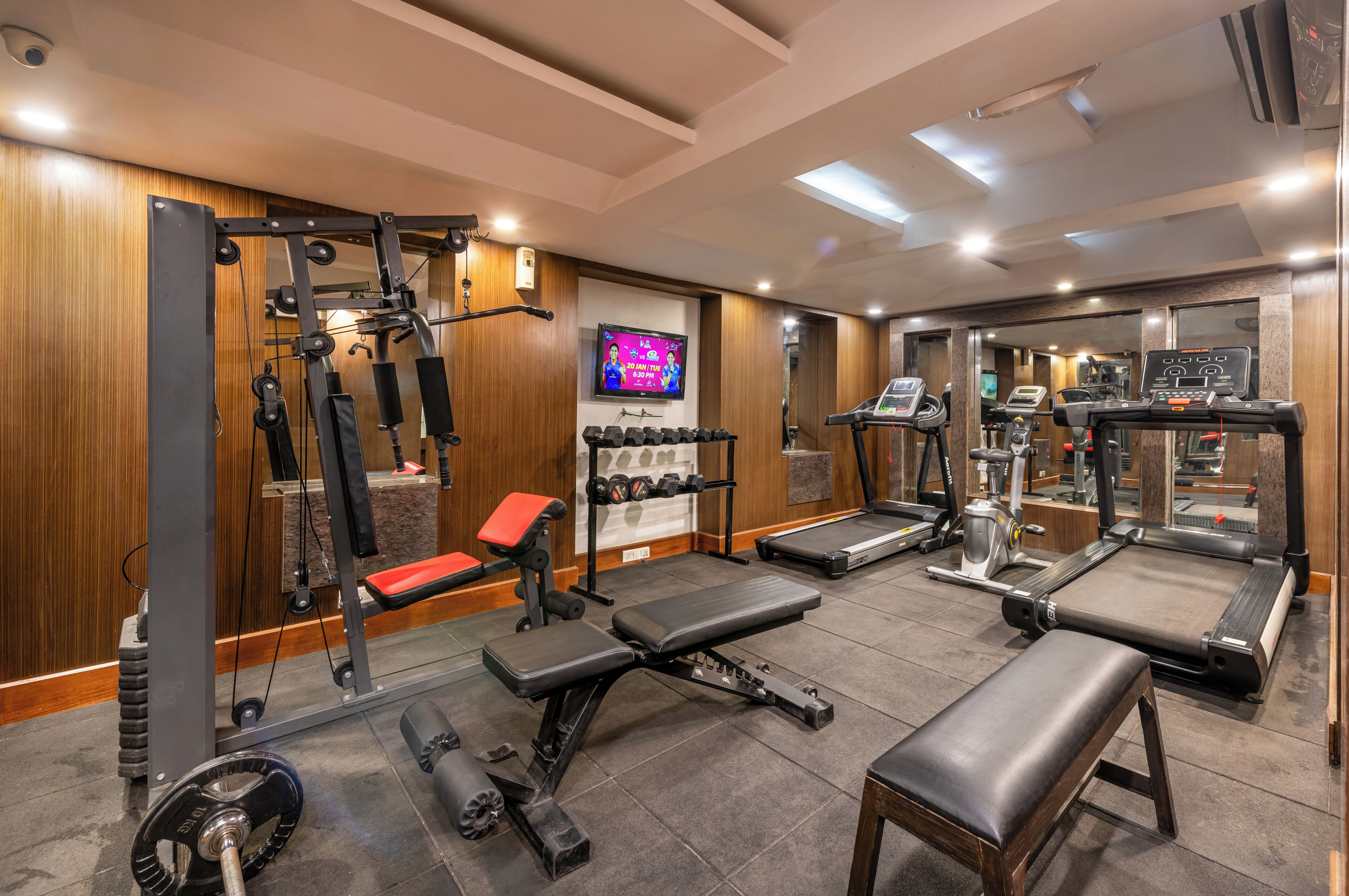 Un gimnasio con equipo de levantamiento de pesas, cintas de correr y una pantalla de televisión.