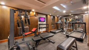 Un gimnasio con equipo de levantamiento de pesas, cintas de correr y una pantalla de televisión.