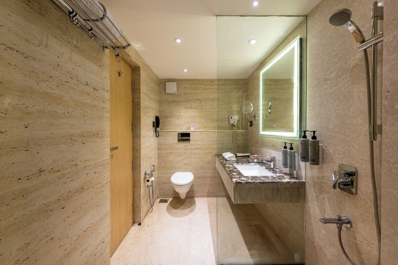A modern bathroom with a marble sink, a glass-enclosed shower, and a wooden door.