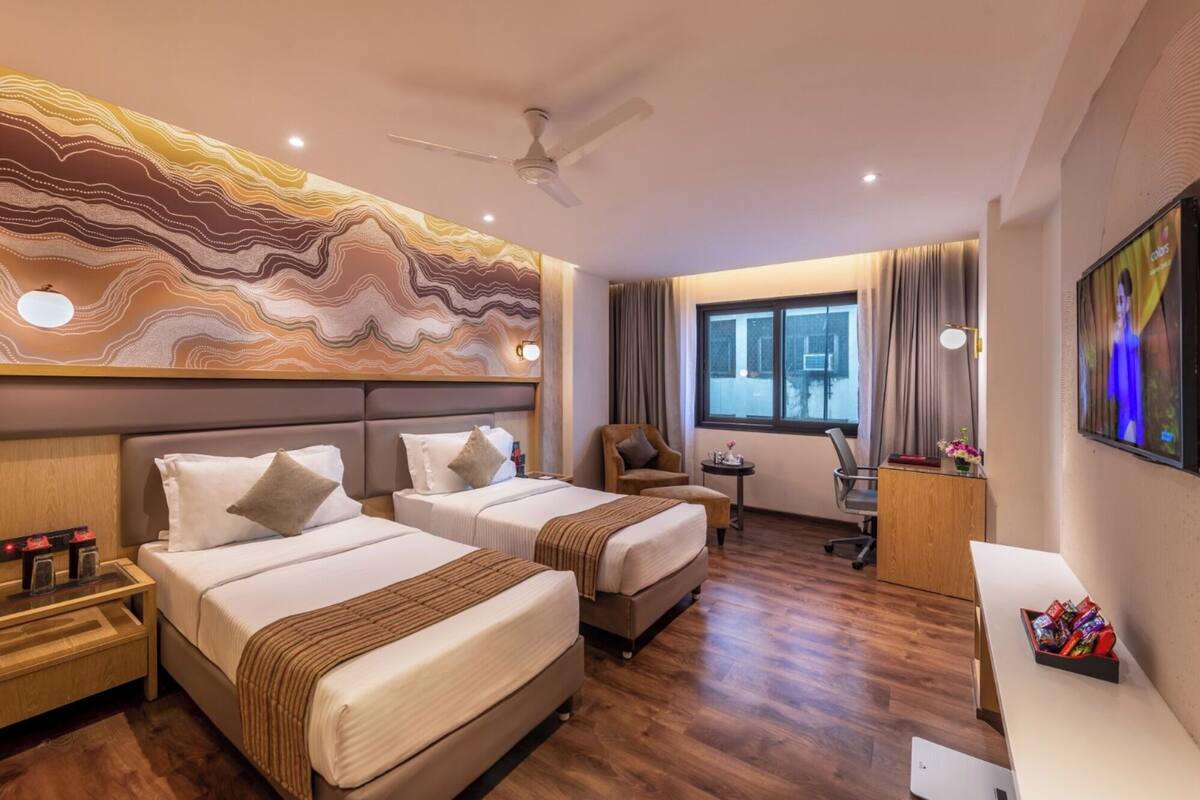 Habitación de hotel con dos camas, un escritorio, una silla, un televisor y un ventilador de techo.