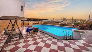 A pool area with a checkered floor, a swing chair, a table with chairs, and a pool ladder. - Lords Plaza, Surat (Surat)