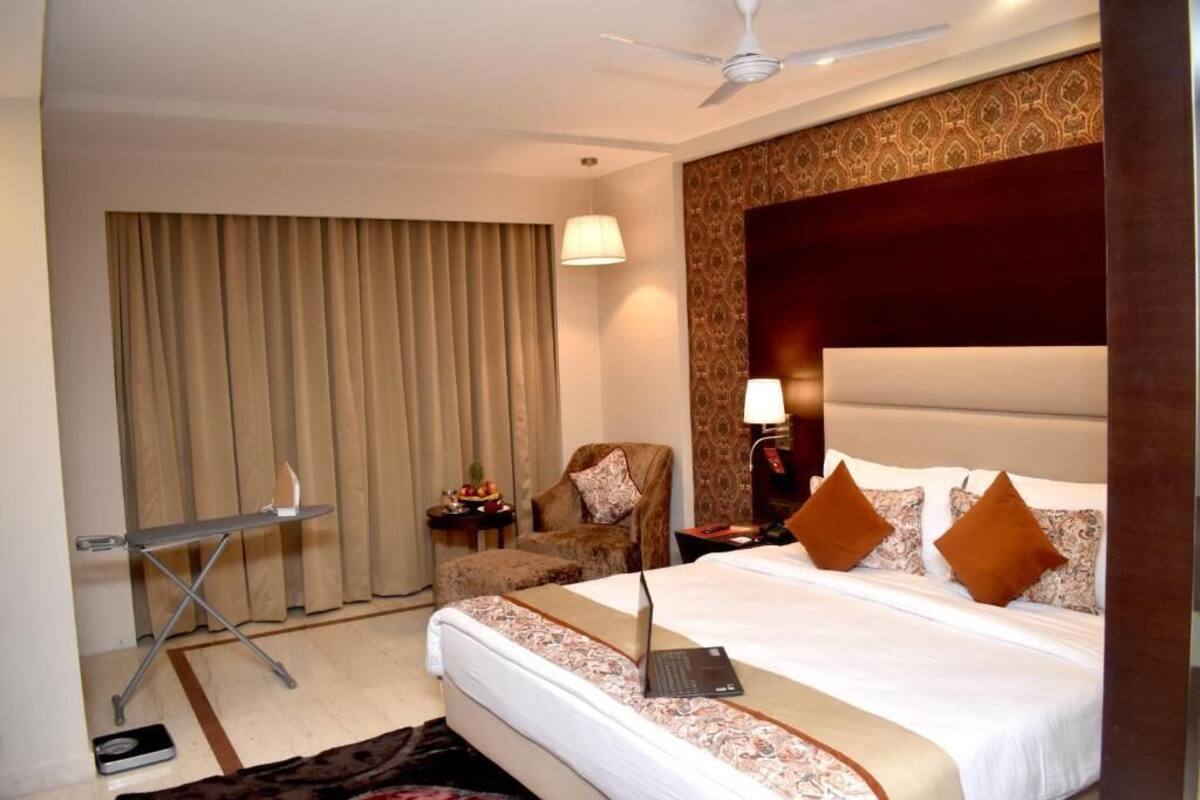 Habitación de hotel con cama, laptop, silla, escritorio y ventilador de techo.