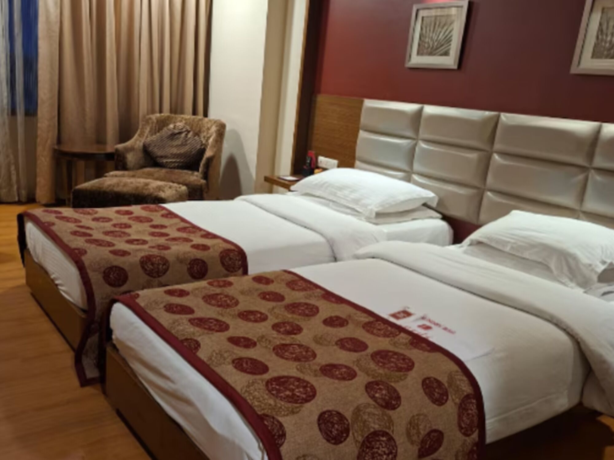 Habitación de hotel con dos camas, una silla, una mesita pequeña y una pared decorada con cuadros.