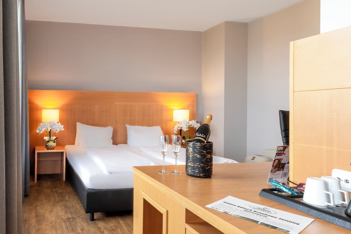 Ein Hotelzimmer mit Bett, Nachttisch mit Champagnerflasche, zwei Gläsern, einer Blumenvase, einer Kaffeemaschine und einer Speisekarte auf dem Tisch.