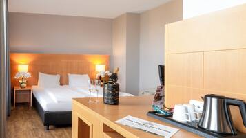 A hotel room with a bed, bedside table with a bottle of champagne, two glasses, a vase with flowers, a coffee maker, and a menu on the table.