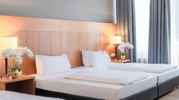 Una habitación de hotel con una cama grande, dos mesitas de noche con lámparas, y vistas al exterior a través de una ventana con cortinas.