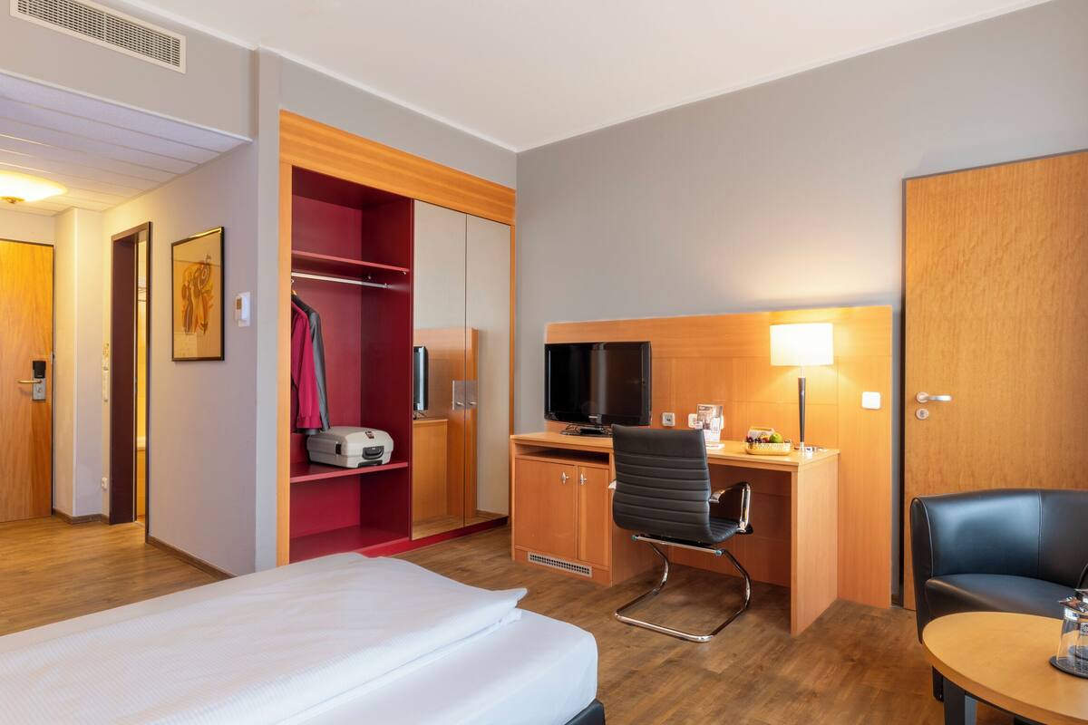 Ein Hotelzimmer mit einem Bett, einem Schreibtisch mit Stuhl, einem Fernseher, einer Lampe und einem Kleiderschrank.