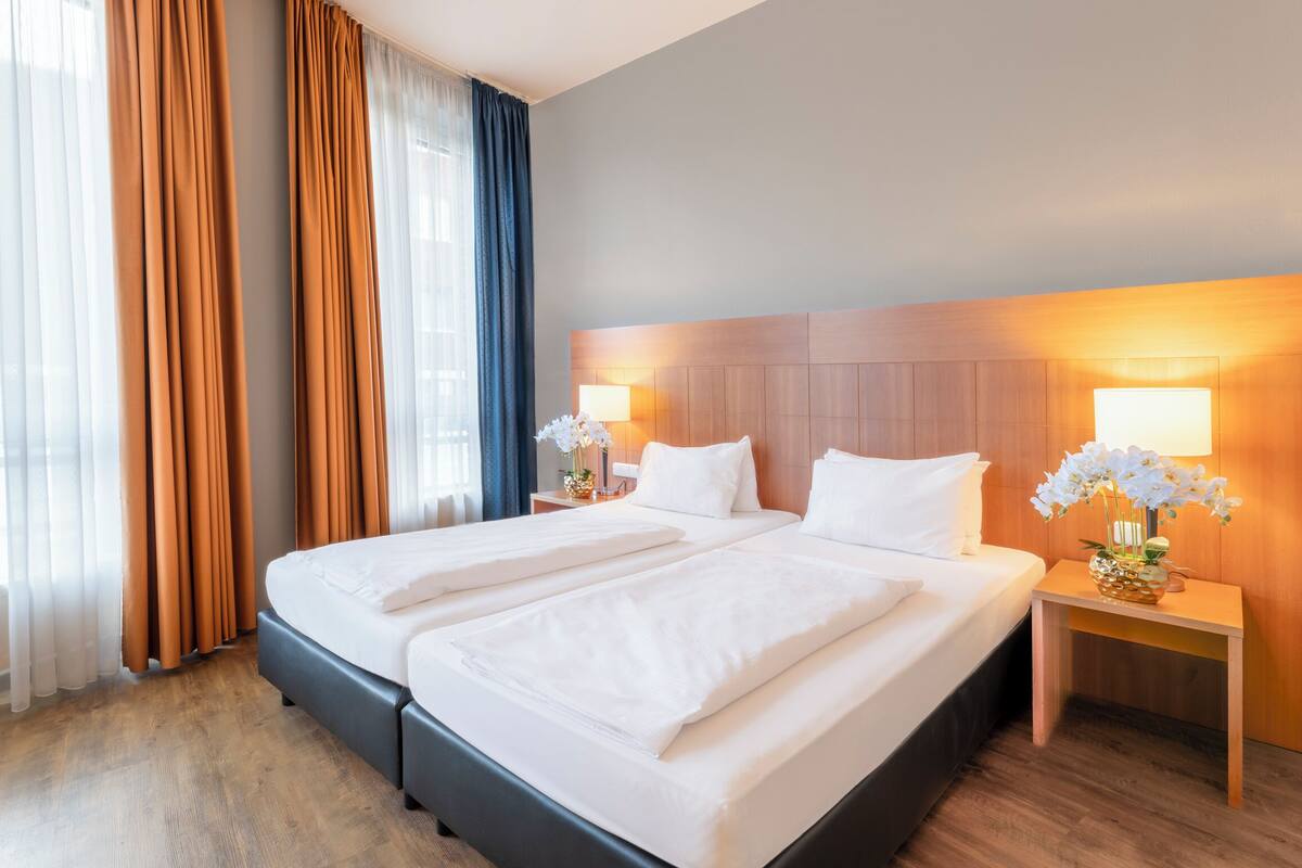 Ein Hotelzimmer mit einem großen Bett, zwei Nachttischen, einem Fenster mit Vorhängen.