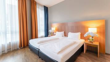 A hotel room with a large bed, two bedside tables, a nightstand, and a window with curtains.