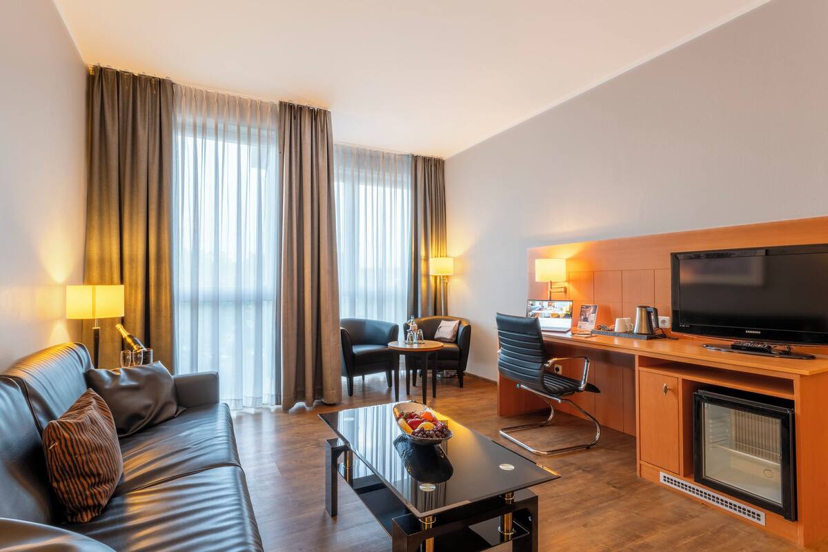 Ein modernes Hotelzimmer mit Ledersofa, Esstisch, Fernseher und Kamin.
