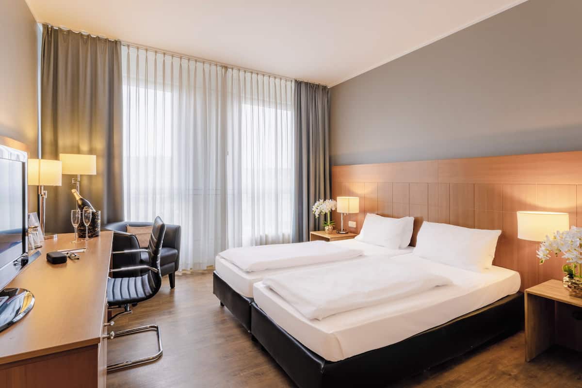 Ein Hotelzimmer mit einem großen Bett, einem Fernseher, einem Schreibtisch mit Stuhl und einem Nachttisch mit Lampe.