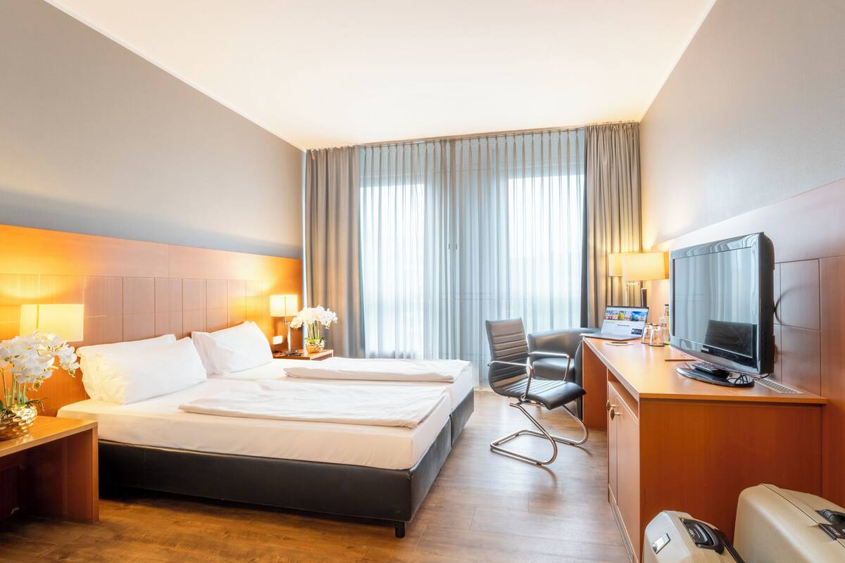 Ein Hotelzimmer mit Bett, Schreibtisch, Fernseher und einem Fenster mit Vorhängen.