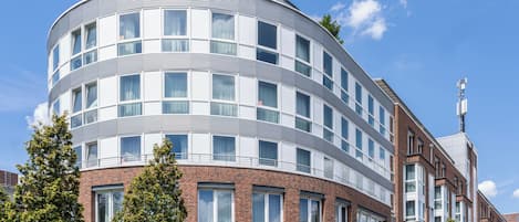A modern, multi-story building with a curved facade, large windows, and a brick base.