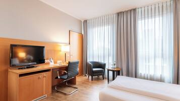 A hotel room with a bed, a desk with a television, a chair, and a small table.