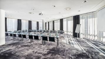 Ein Konferenzraum mit Tischen, Stühlen, großen Fenstern mit Vorhängen und einem Whiteboard-Ständer.