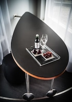 Una mesa de comedor moderna y redonda, con superficie negra y patas metálicas, adornada con una botella, copas y una bandeja de uvas y manzanas.