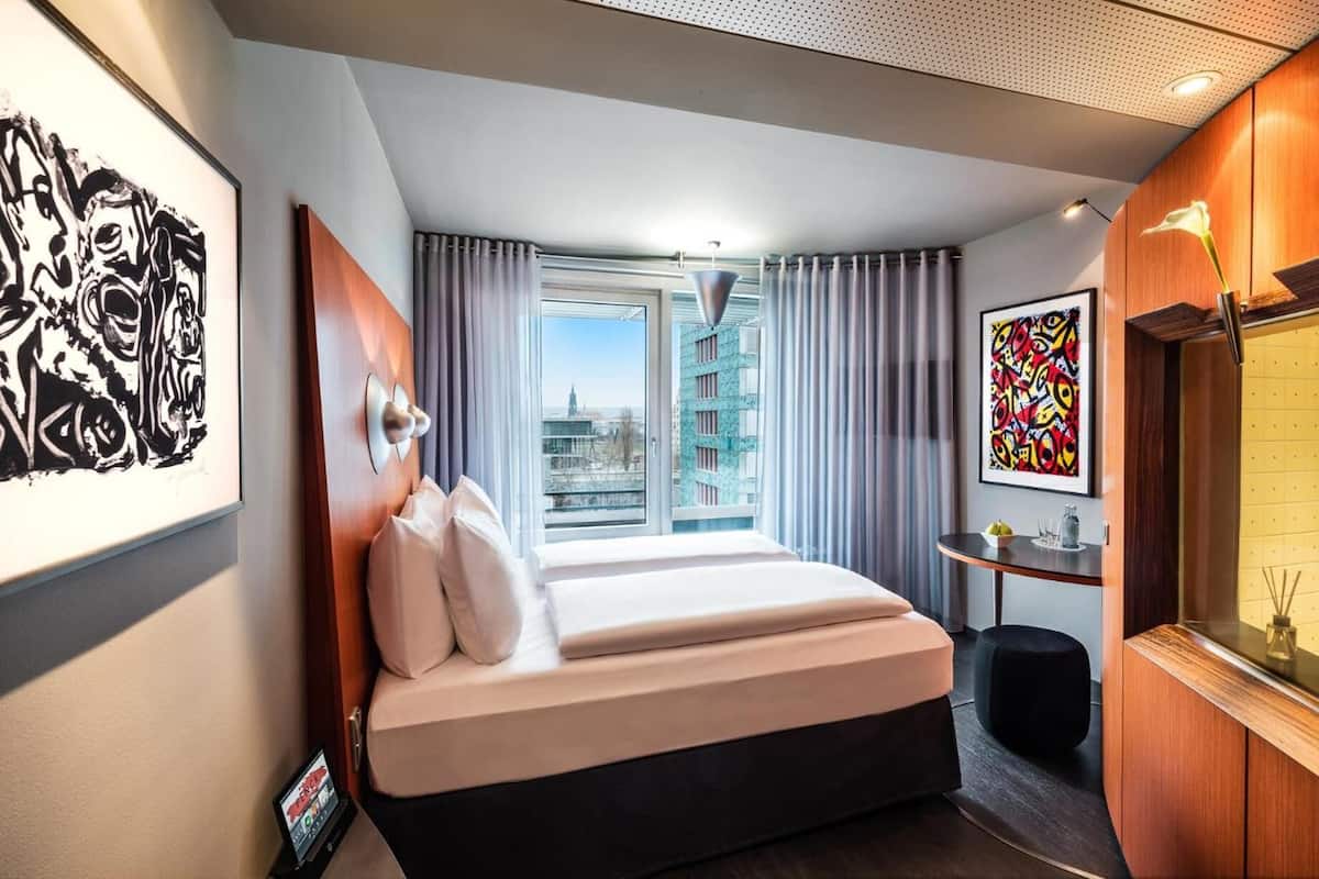 Una habitación de hotel moderna con una cama grande, un escritorio con lámpara y obras de arte en las paredes.