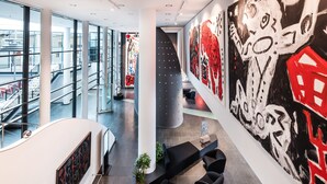 A modern interior with a curved white wall, a large abstract mural, and a seating area with black furniture. - Penck Hotel Dresden (Dresden)