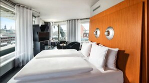 A hotel room with a large bed, a wooden accent wall, a TV, and a view of a cityscape. - Penck Hotel Dresden (Dresden)