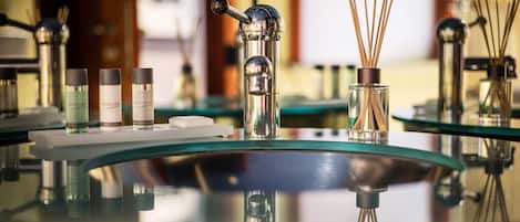 Une salle de bain moderne avec un lavabo en verre, des produits de soins pour le corps et des diffuseurs à bâtonnets.