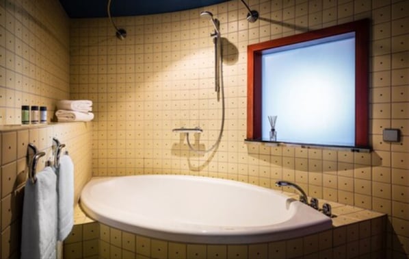 A bathroom with a large bathtub, a shower, and a window above the sink. - Penck Hotel Dresden (Dresden)
