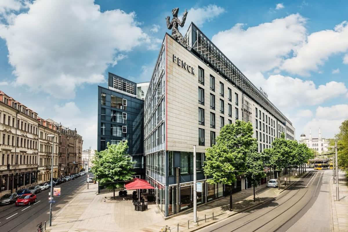 Un edificio moderno con un llamativo letrero que dice "FENCK", fachada de vidrio y una línea de tranvía cerca.