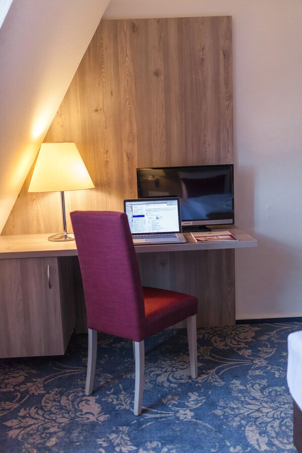 Una habitación con escritorio, ordenador portátil, televisor, lámpara y silla.