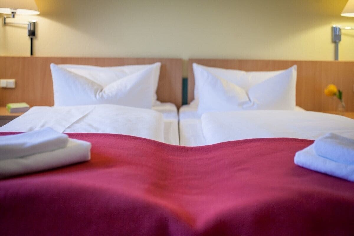 A hotel room with two beds, each with white linens and a red bedspread.