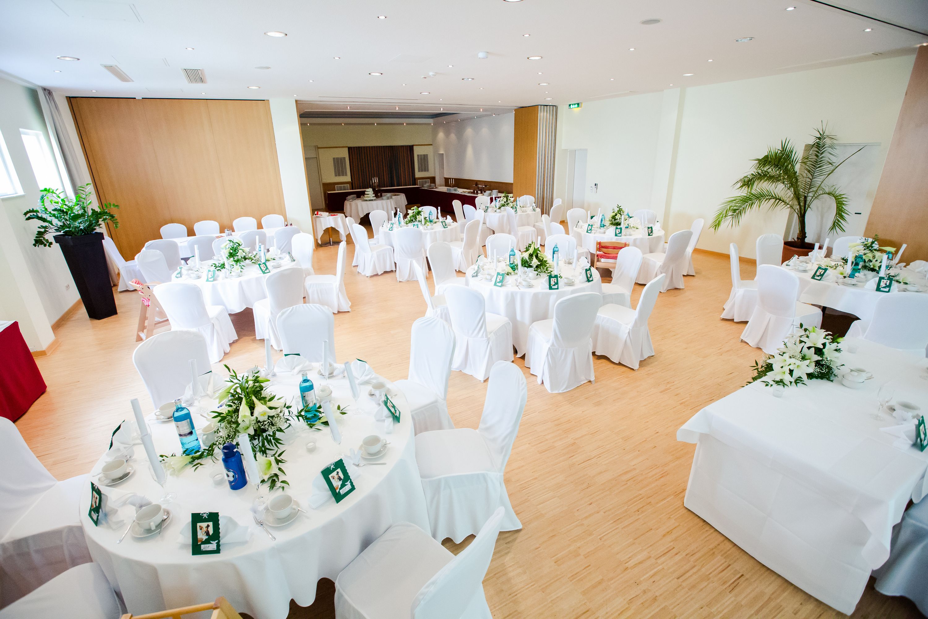 A banquet hall with round tables set for a formal event, featuring white tablecloths and chairs, and floral centerpieces.