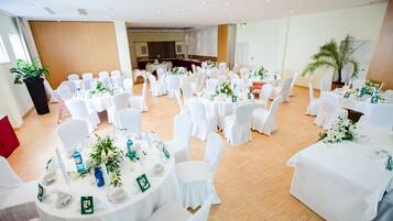 A banquet hall with round tables set for a formal event, featuring white tablecloths and chairs, and floral centerpieces.