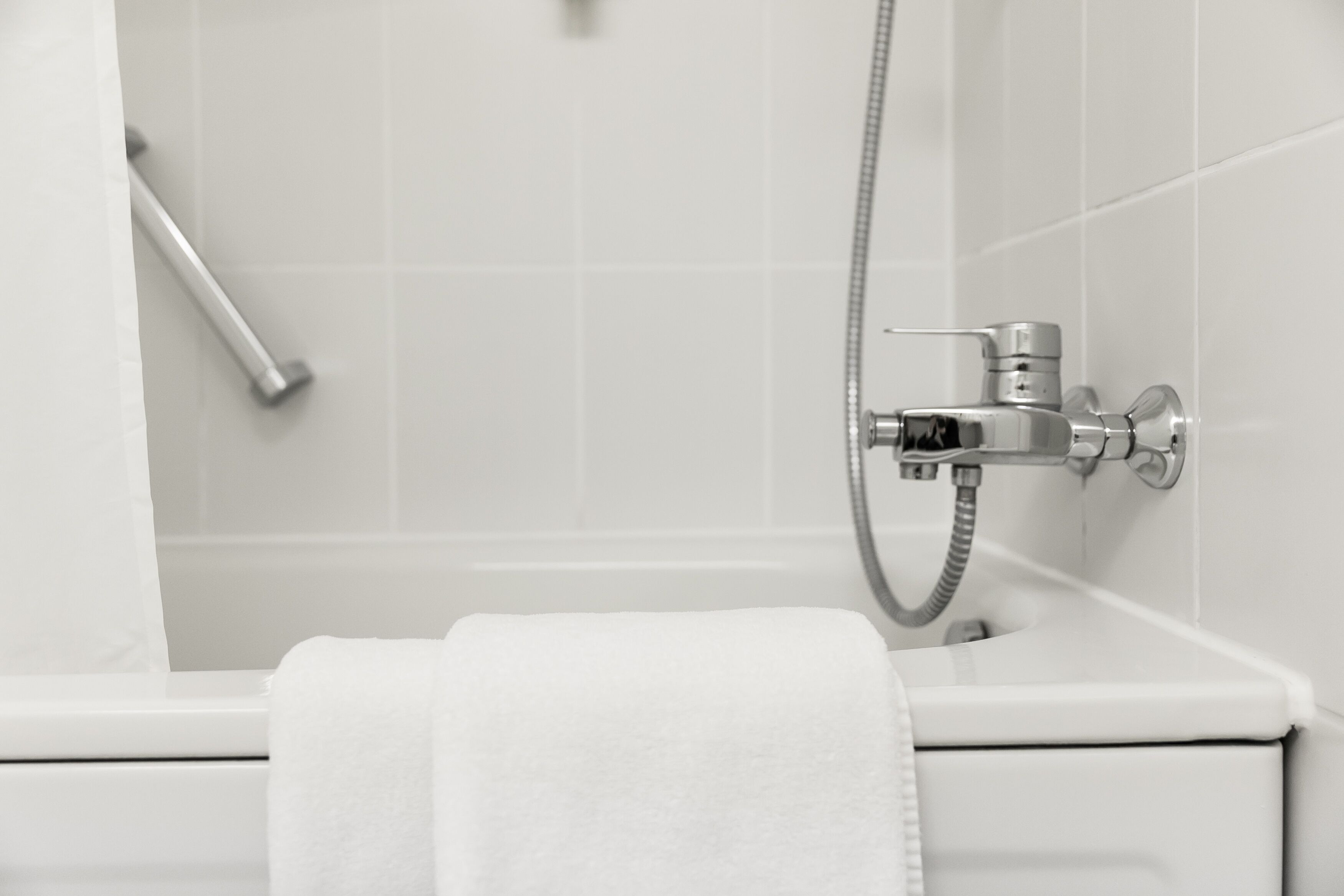 Un baño con una bañera blanca, un cabezal de ducha manual y una toalla colgada al lado.