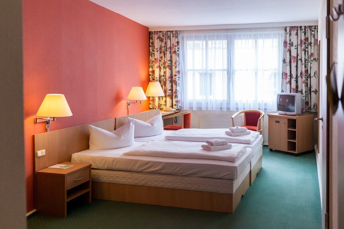 Ein Hotelzimmer mit einem großen Bett, zwei Nachttischlampen, einem Fernseher und einem kleinen Schreibtisch.