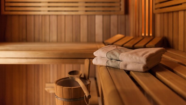 A sauna room with wooden benches, a towel, and a wooden bucket. - TOP martas Hotel Lutherstadt-Wittenberg (Lutherstadt Wittenberg)