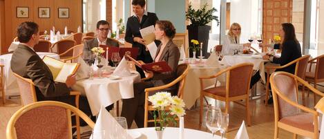Un restaurant avec des tables rondes, des nappes blanches et des chaises en bois.
