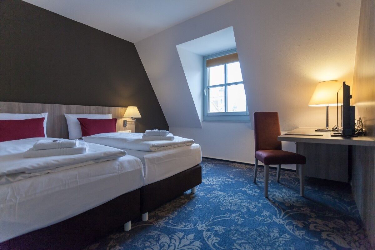 A hotel room with two beds, a desk, a chair, and a window.