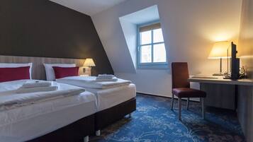 A hotel room with two beds, a desk, a chair, and a window.
