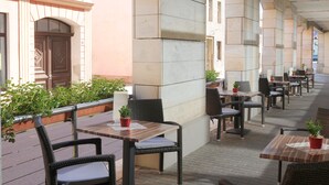 An outdoor cafe with wicker chairs and tables, potted plants, and a brick floor. - TOP martas Hotel Lutherstadt-Wittenberg (Lutherstadt Wittenberg)