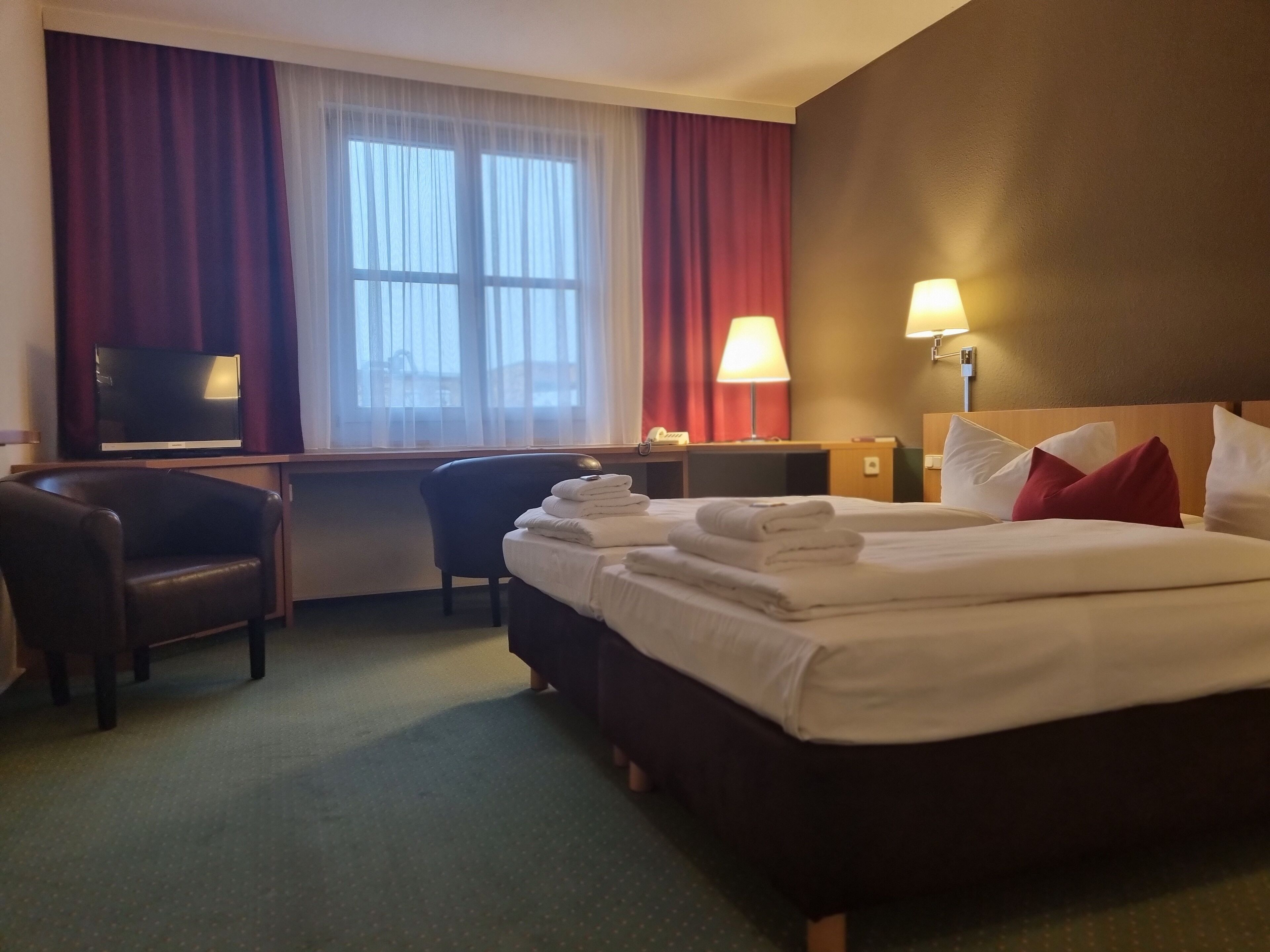 A hotel room with a bed, a desk, a chair, a TV, and a lamp.