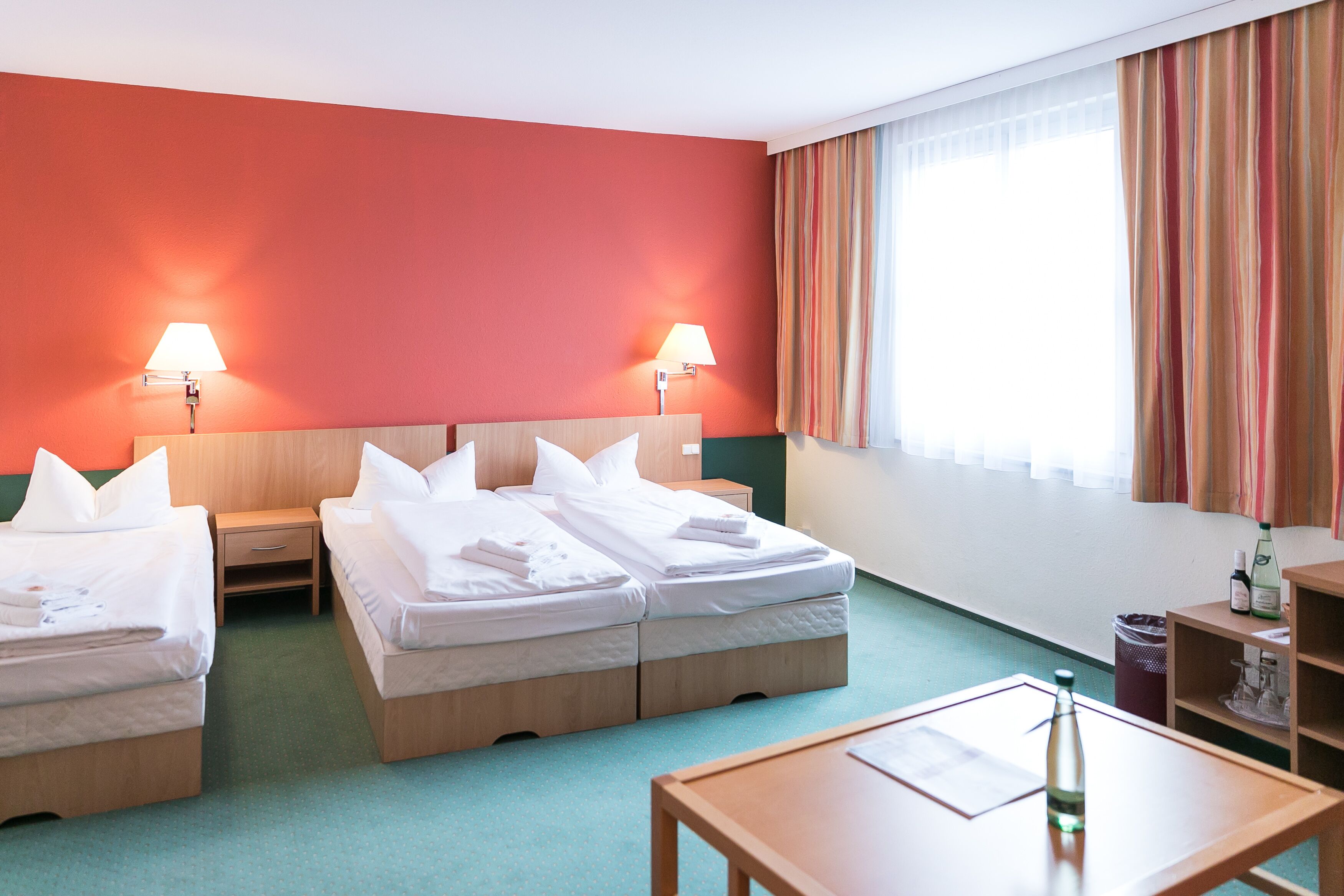 Habitación de hotel con dos camas, un escritorio y una ventana con cortinas.