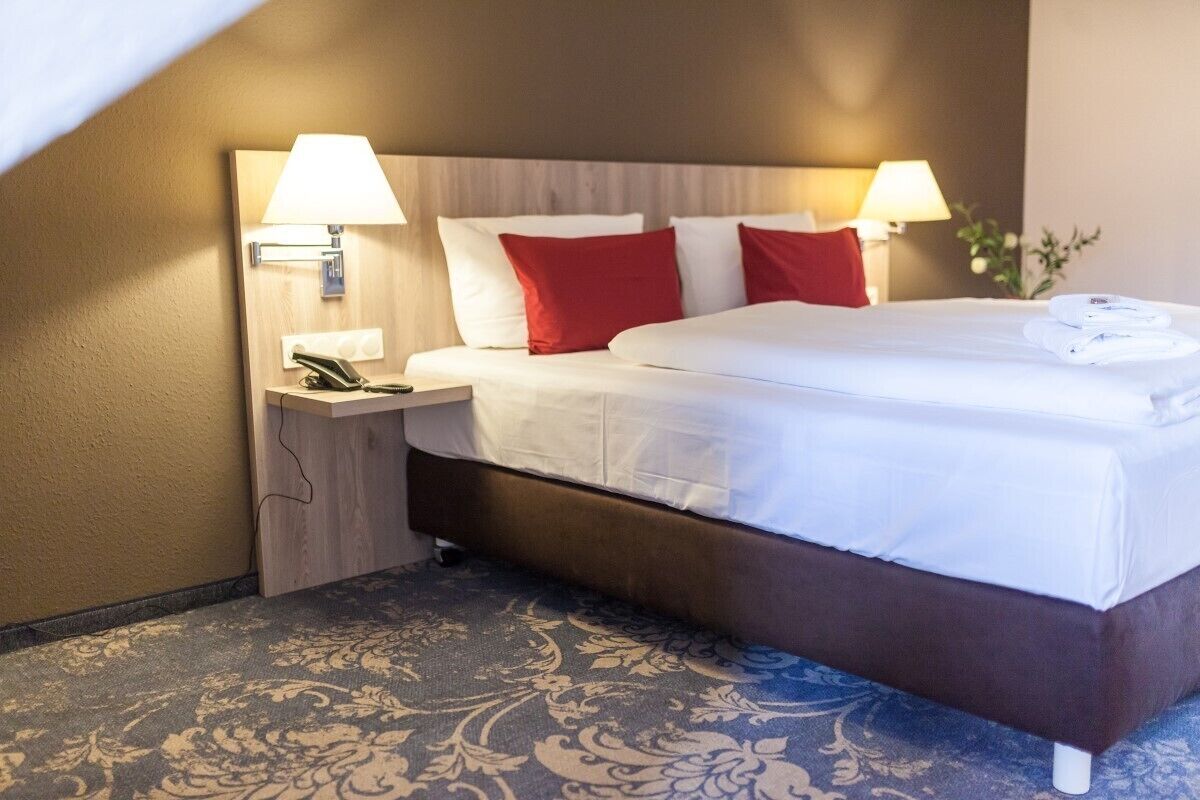 Une chambre d’hôtel avec un grand lit, deux lampes de chevet, une table de chevet avec un téléphone et une moquette à motifs floraux.
