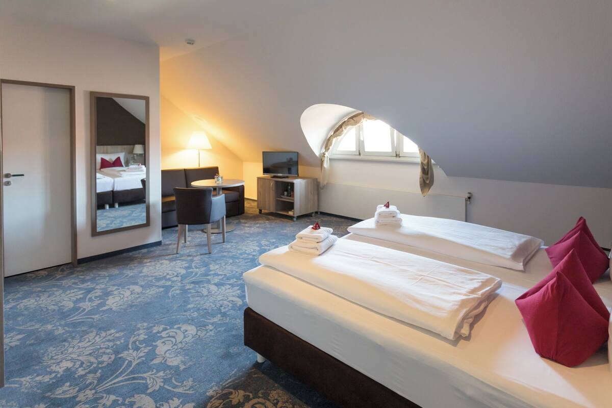 Quarto de hotel com duas camas, uma escrivaninha, uma cadeira, televisão e um espelho grande.