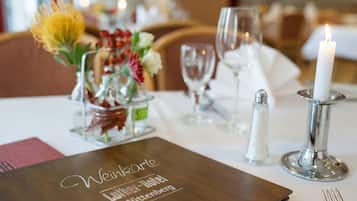 Una mesa dispuesta con un menú, velas, saleros y pimenteros, y un centro de mesa floral.