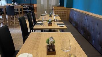 Un comedor con mesas de madera, sillas negras y paredes azules.