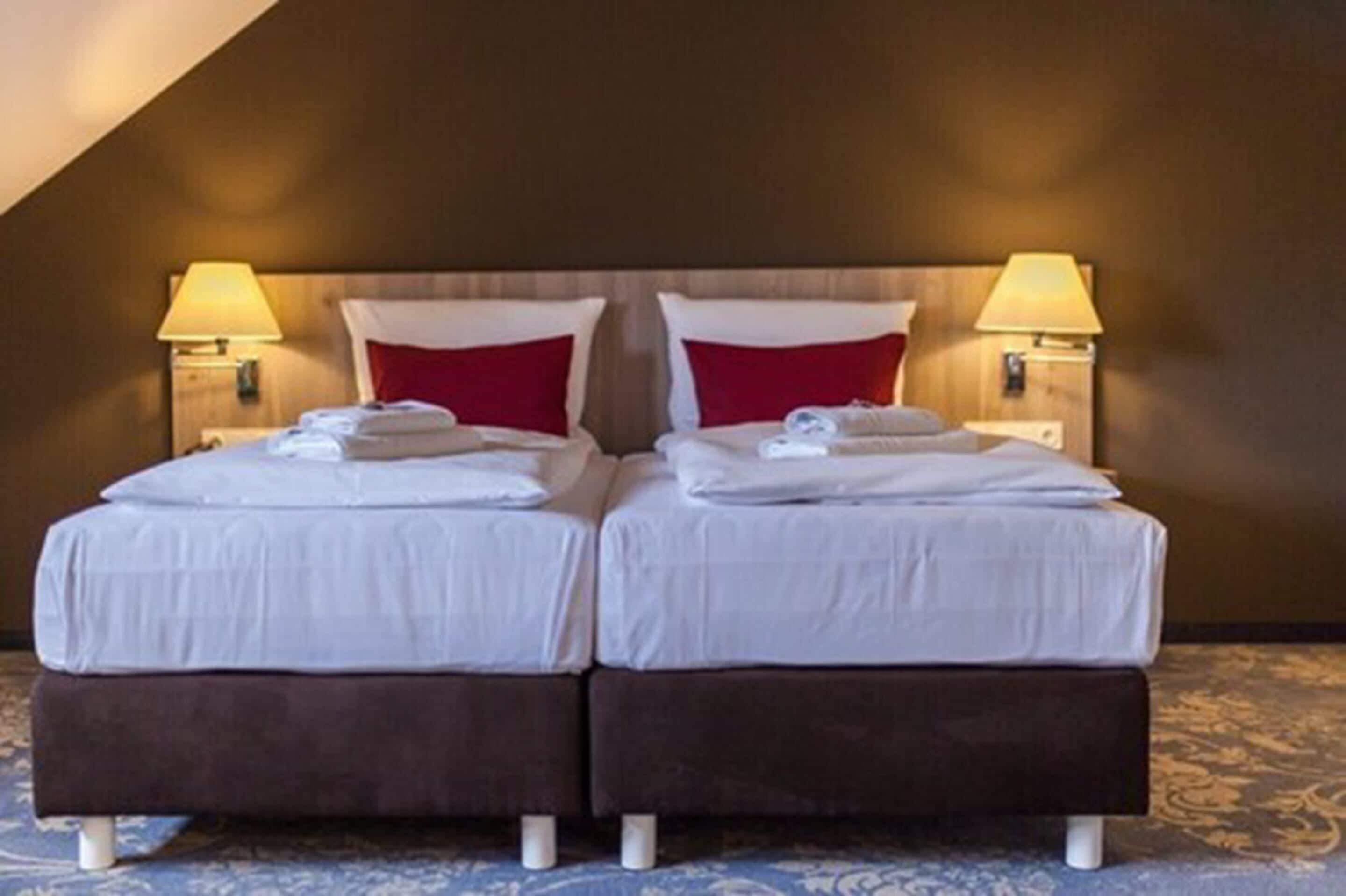 Ett hotellrum med två sängar, båda med vita lakan och röda kuddar, och två sänglampor.