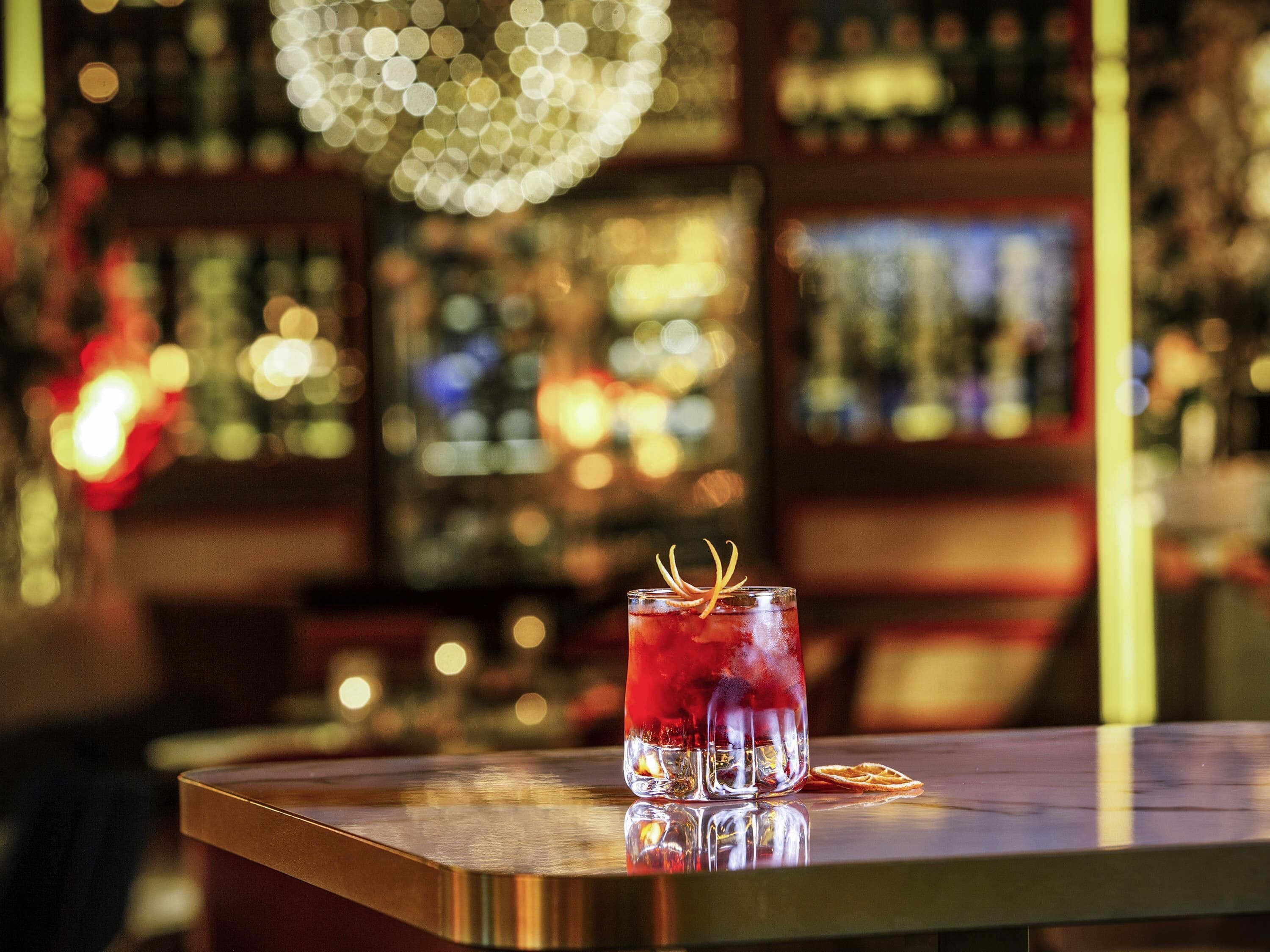 Un bar con una copa de bebida roja, una barra de madera y una araña.