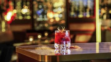 Un bar con una copa de bebida roja, una barra de madera y una araña.