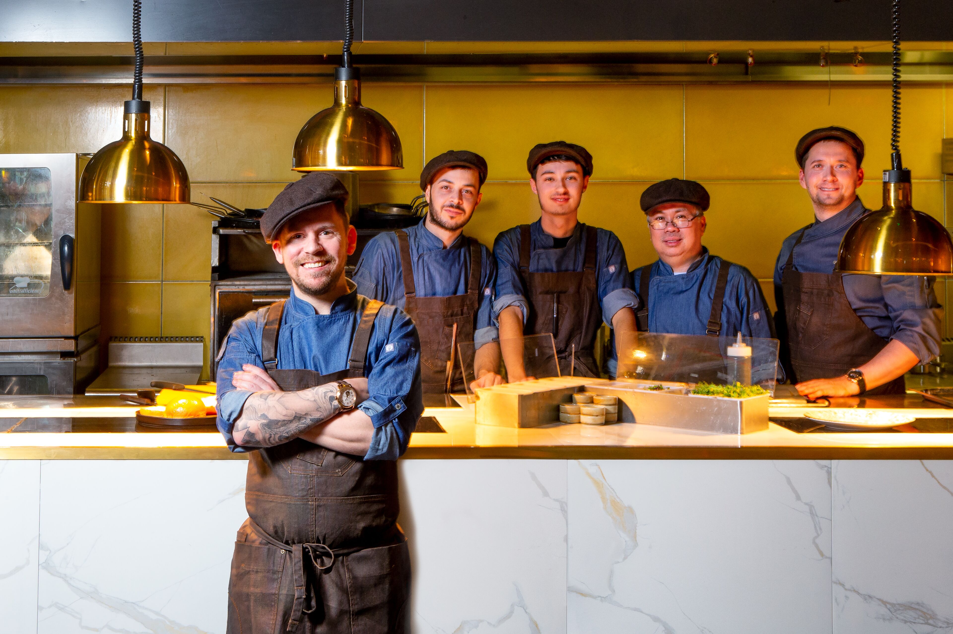Un grupo de cocineros en una cocina con encimeras de mármol e iluminación colgante.