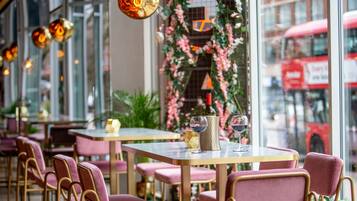 Interior de restaurante con mesas y sillas, un arreglo floral decorativo y una botella de vino sobre una mesa.